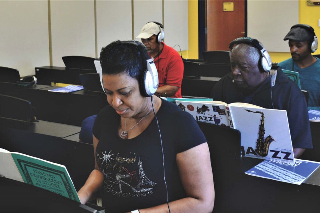 Four adults wearing headphones and playing electronic pianos. 