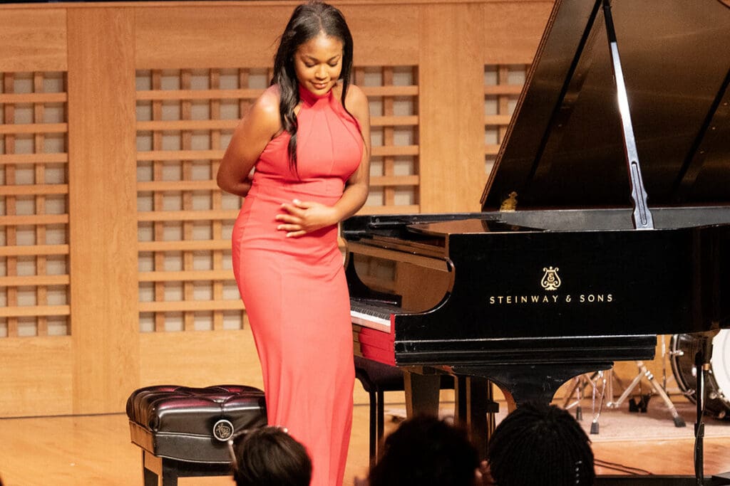 Person in red dress taking a bow in front of piano.