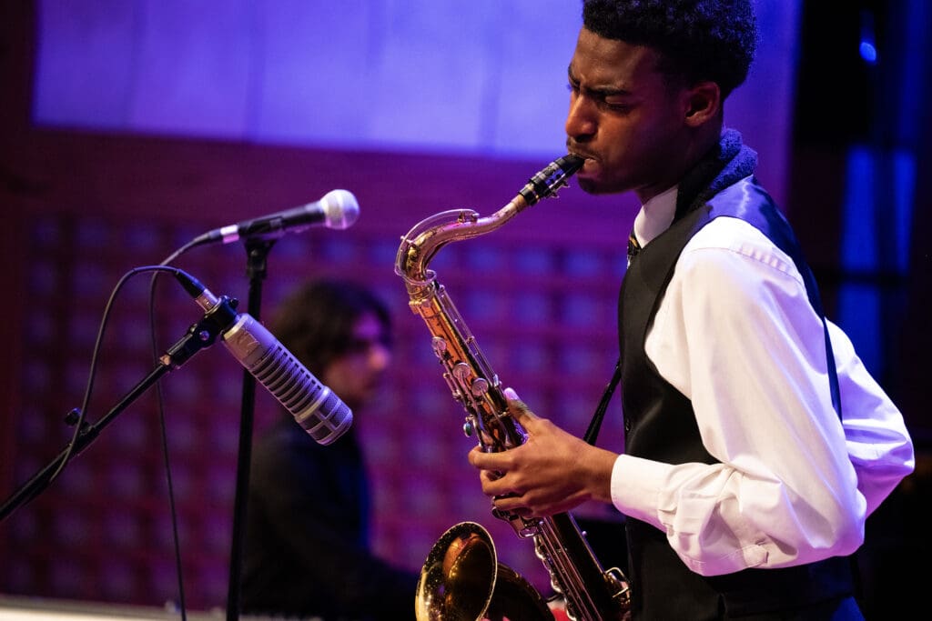 Person in suit on stage playing saxophone.