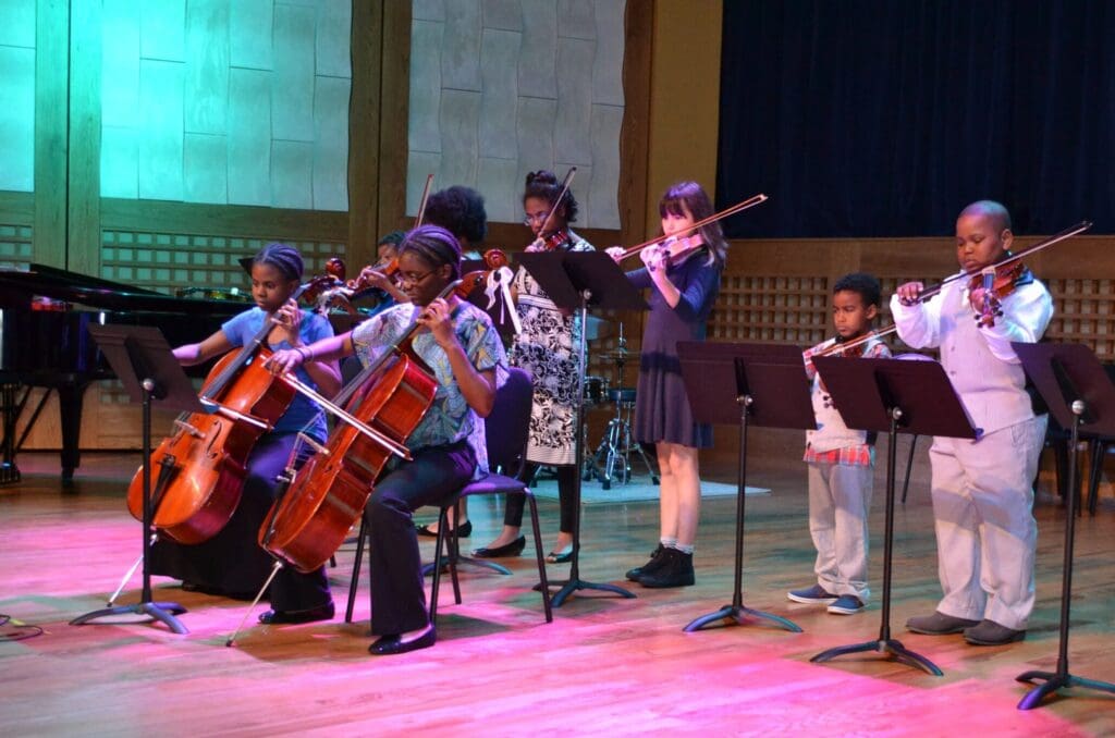 Children playing a variety of instruments on stage.